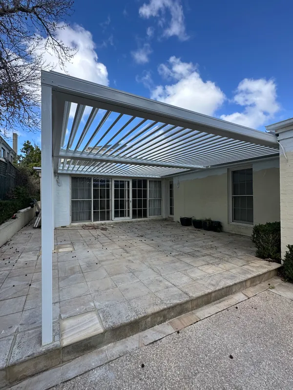 Wide white louvred roof spanning an established courtyard