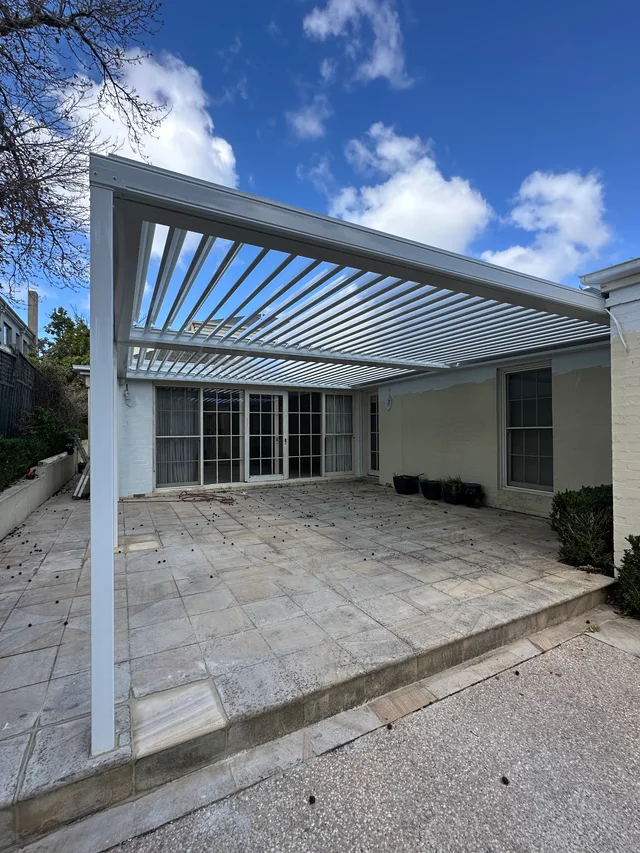Wide white louvred roof spanning an established courtyard